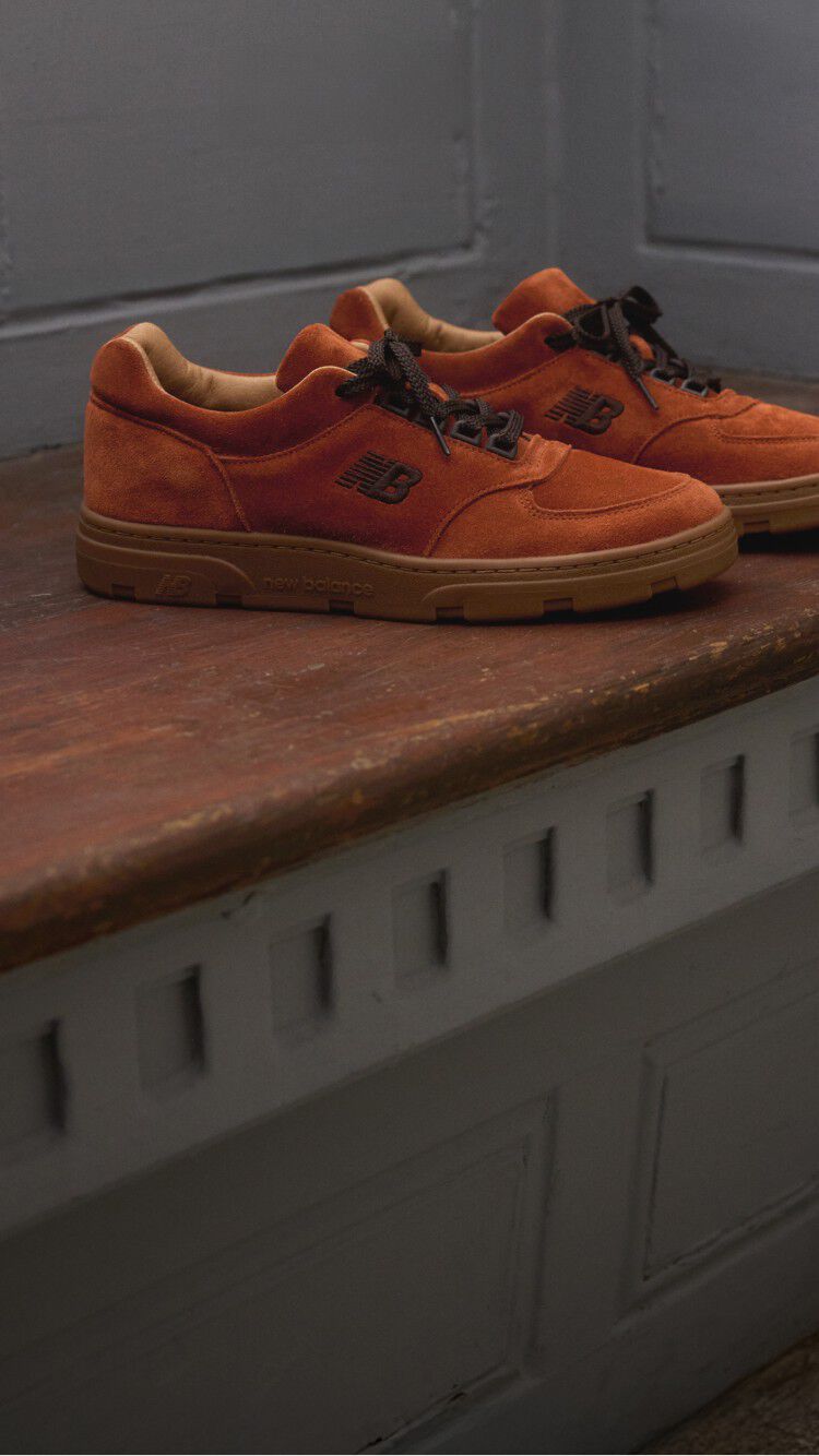 A pair of New Balance Made in UK sneakers sitting on a wooden window seat with panel detailing on the walls.